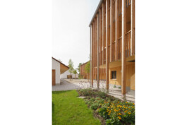 Außenansicht des Laubengangs mit unterschiedlich dichter vertikalerholzlattung, mit Darstellung der Außenanlagen, BEgrünung und befestigter Hof