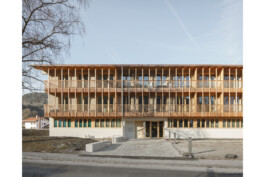 Hofansicht des kommunanlen Wohnungsbaus in Oberau. Erdgeschoss in MAssivbauweise sichtbar, ab dem Obergeschoss mit Holz verkleidet in vertikaler Struktur