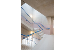 Treppenhaus in Beton mit farbigem Handlauf in blau und teilweise rosafarben beschichteter Treppenhauswand