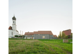 Ansicht des gesamten Hofensembles mit Kirche, Wiese im Vordergrund,vorvergraute Holzverschalung